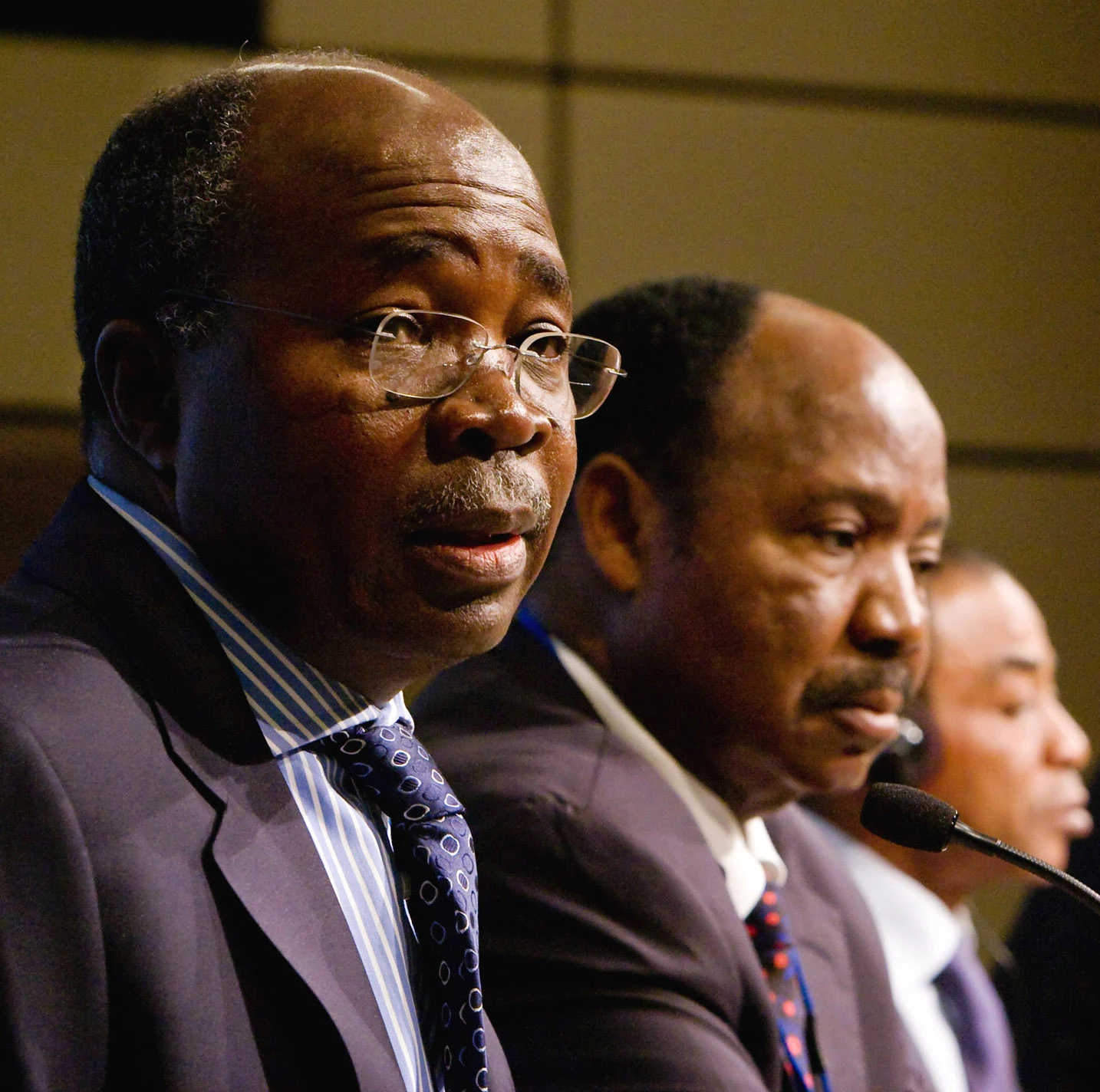 An African finance minister, wearing glasses, speaks at a conference podium.