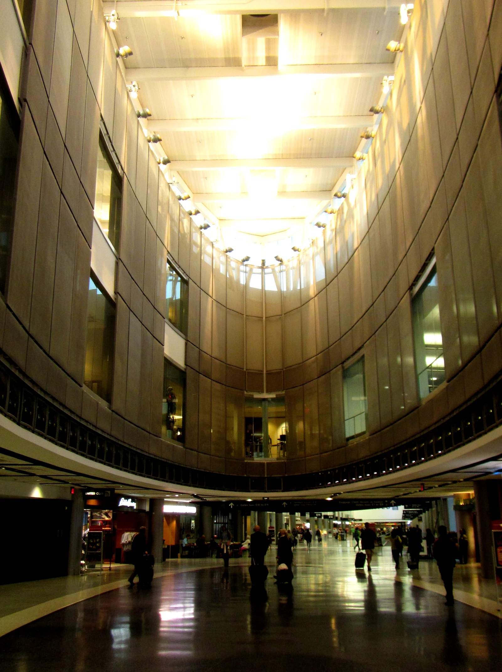 Travelers with luggage walk through the brightly lit George Bush Intercontinental Airport Terminal E.