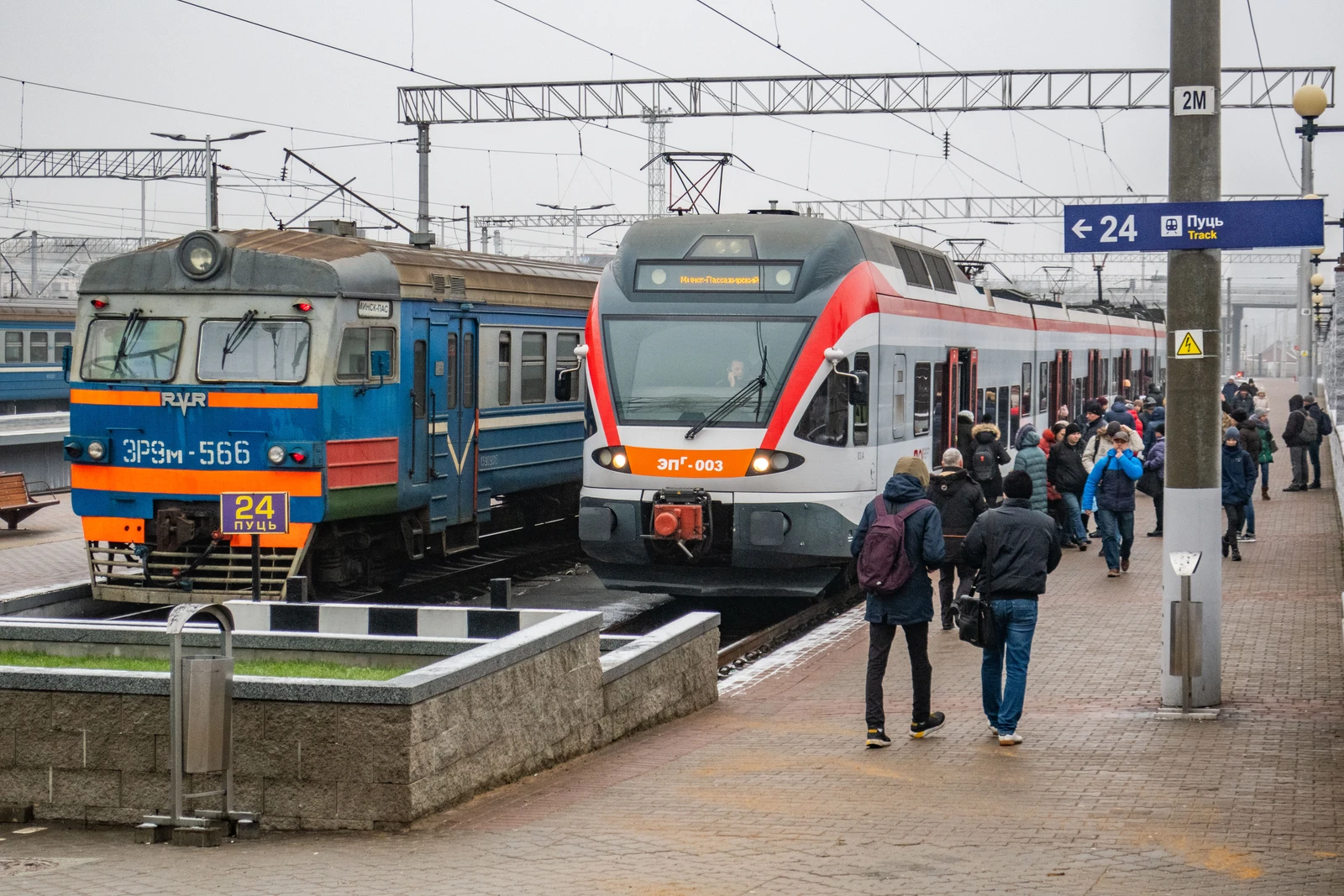 Two passenger trains, an older blue model and a newer red and white model, at a railway station.