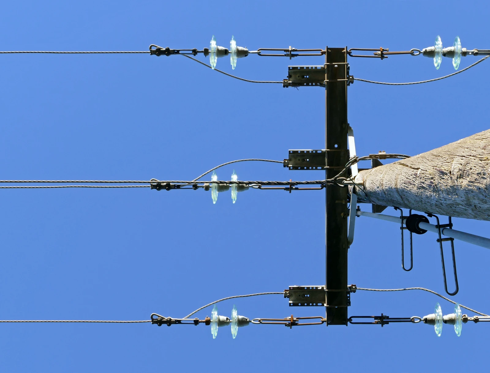 Power lines and insulators attached to the top of a utility pole against a blue sky.