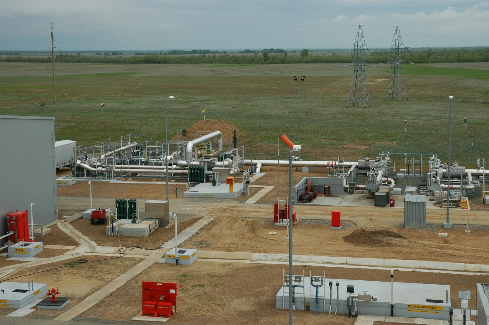 Bolshoi Chagan pumping station infrastructure with pipes, small buildings, and power lines against a field.