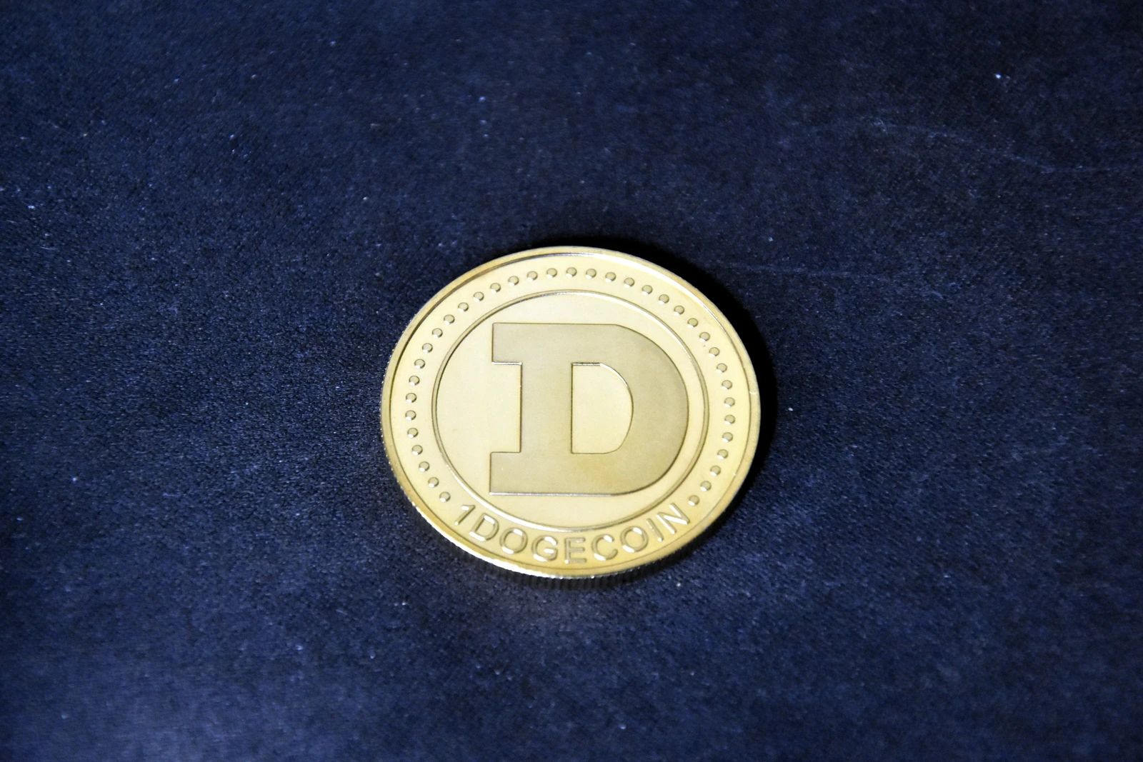 Golden physical Dogecoin with a 'D' on one side resting on a dark surface.