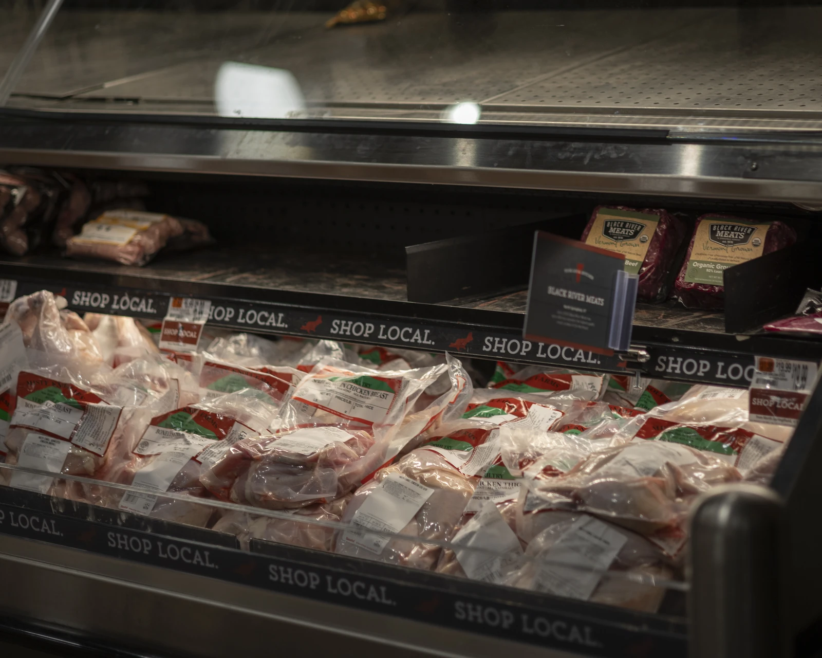 Packaged chicken and beef products in a refrigerated display case inside a grocery store.