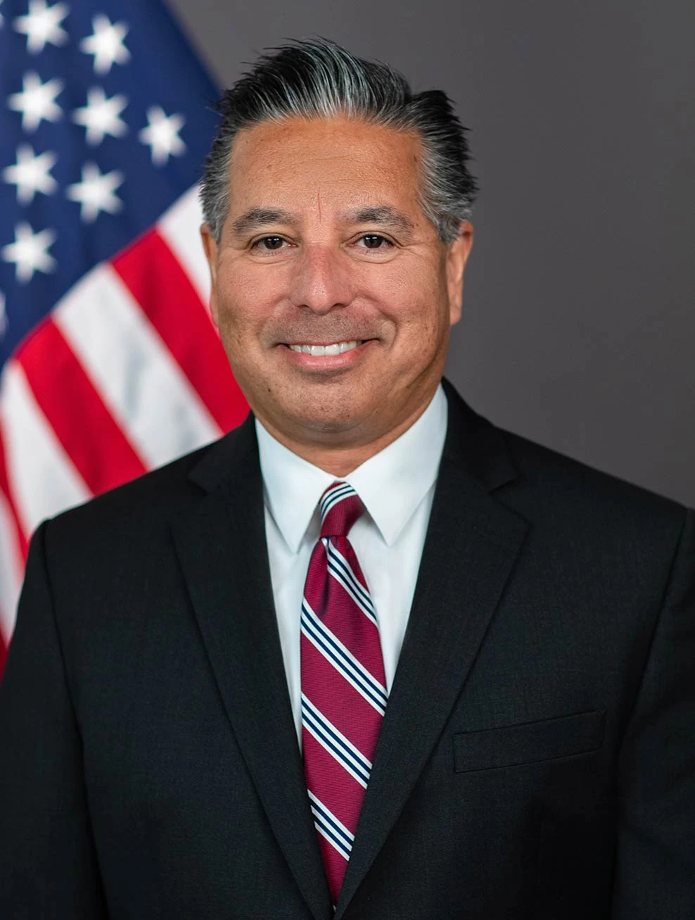 Jaime Lizarraga, SEC Commissioner, smiling in an official portrait against an American flag.
