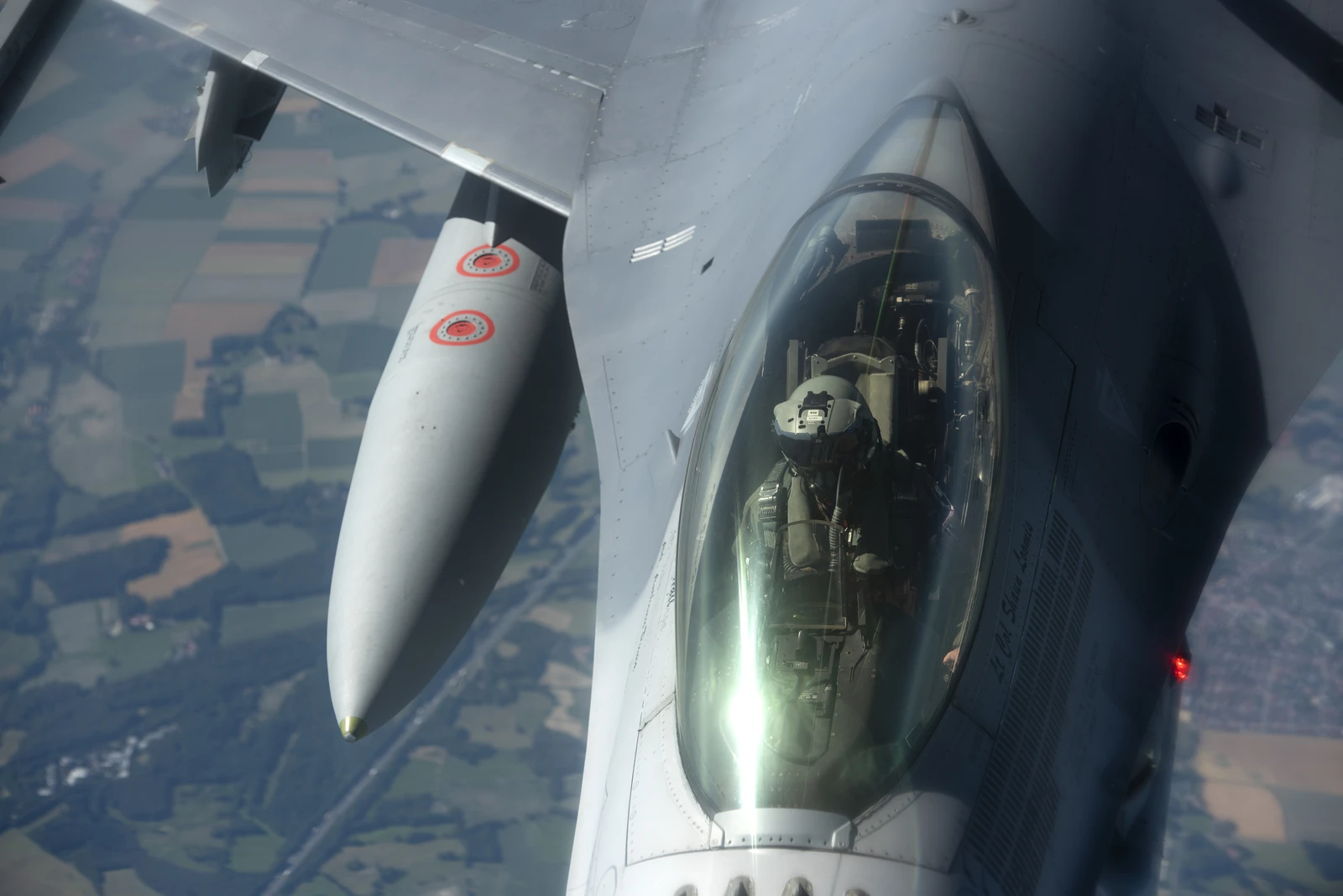Pilot wearing a helmet and oxygen mask in the cockpit of a US Air Force fighter jet.