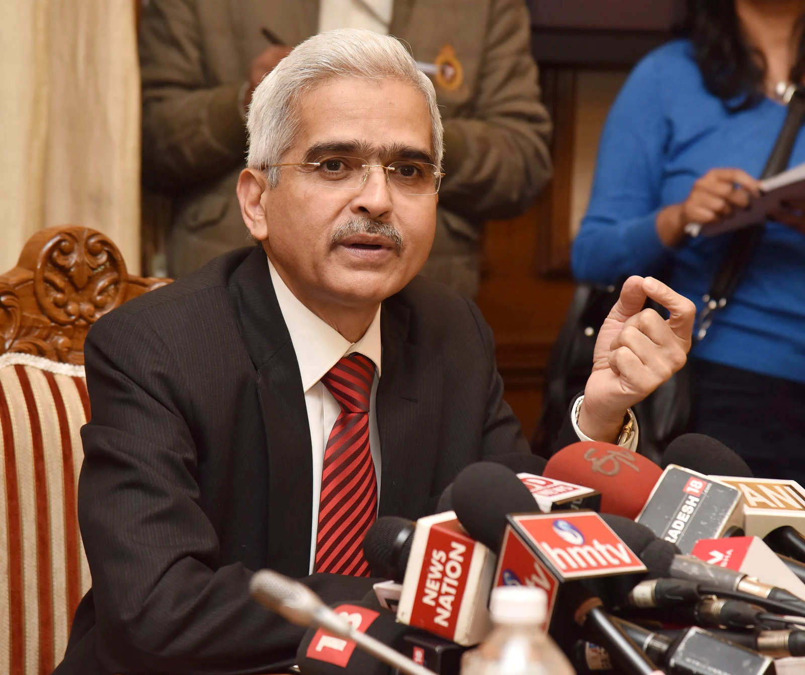 Shaktikanta Das, IAS, speaking at a podium with several news microphones.