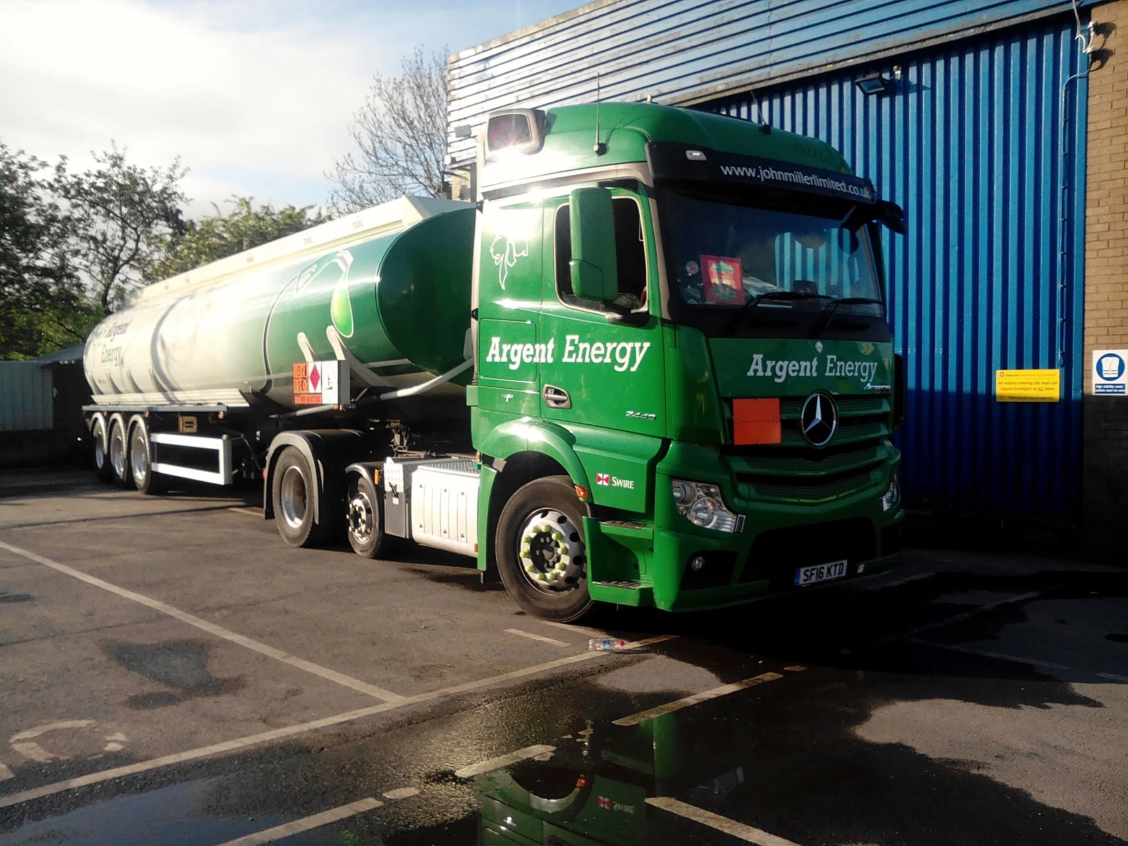 Green Mercedes Benz fuel tanker truck parked at a bus depot.