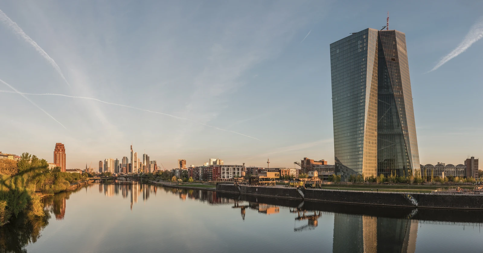The European Central Bank building and other skyscrapers in Frankfurt, Germany, reflecting in a river at dawn.