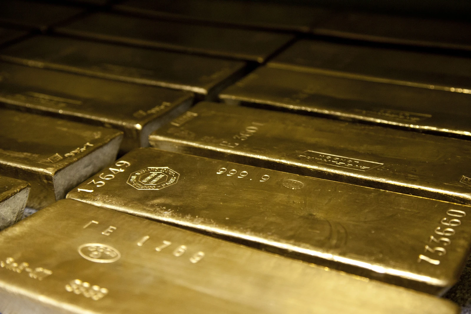 Many 400-ounce gold bars stacked together, showing various stamps and serial numbers.
