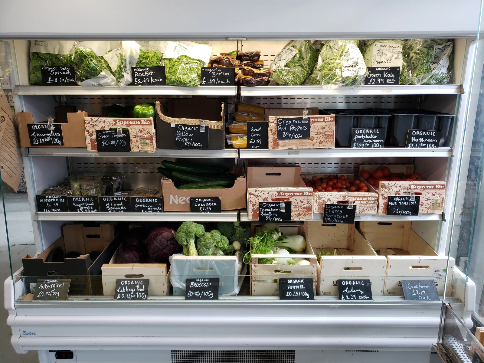 Produce section in a store displaying organic spinach, peppers, tomatoes, and other fresh vegetables.