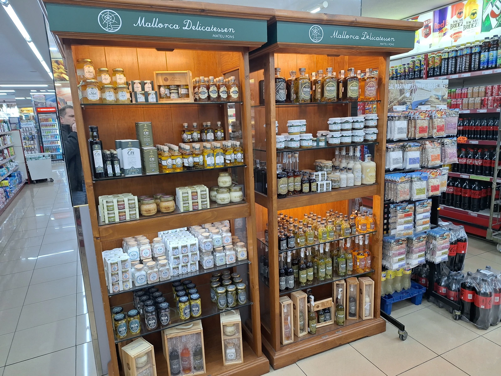 Delicatessen products, including honey, olive oil, and spirits, displayed in a wooden cabinet inside a supermarket.