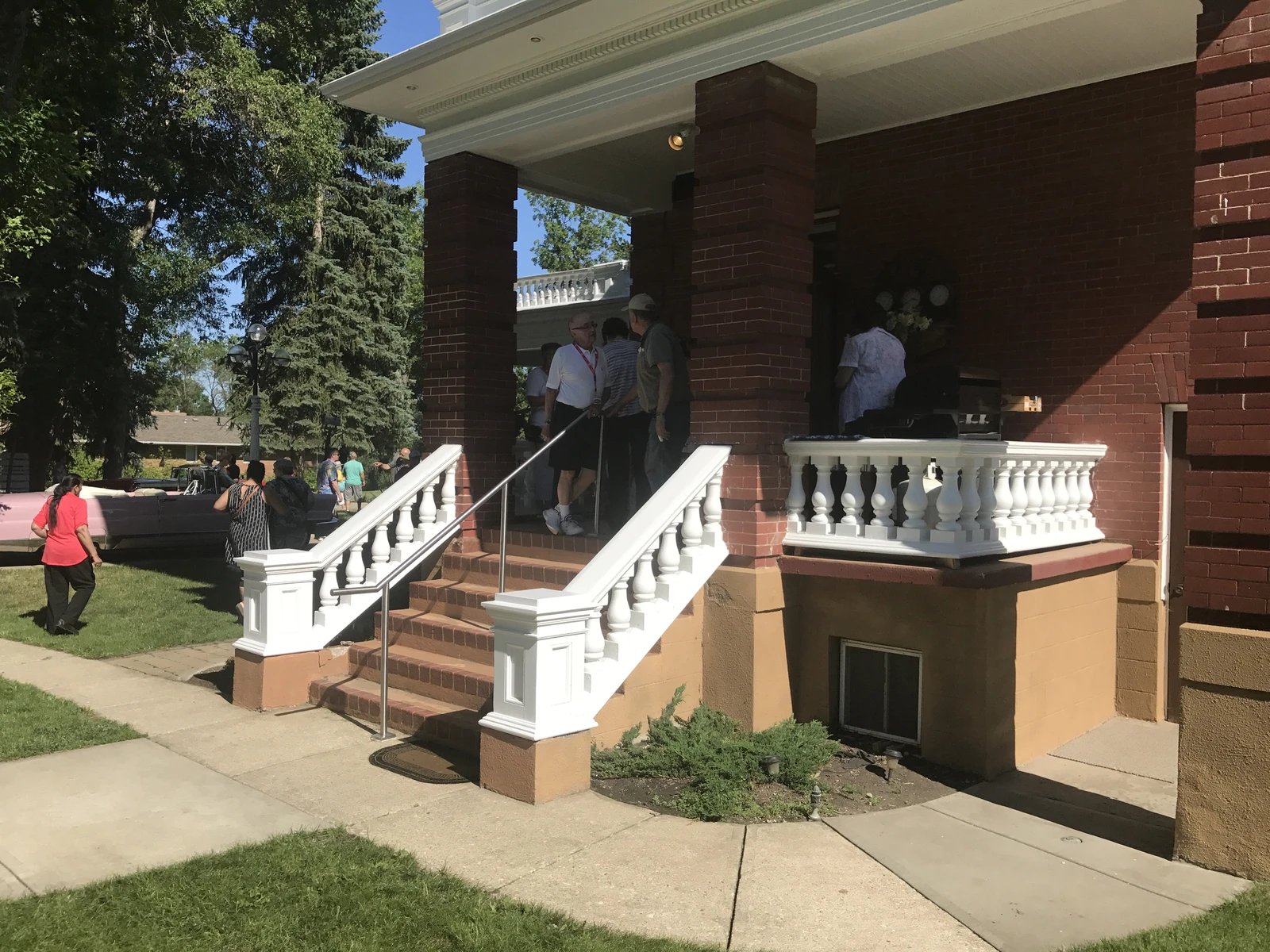 People gathered on the porch and lawn of Magrath Mansion, a brick residence.