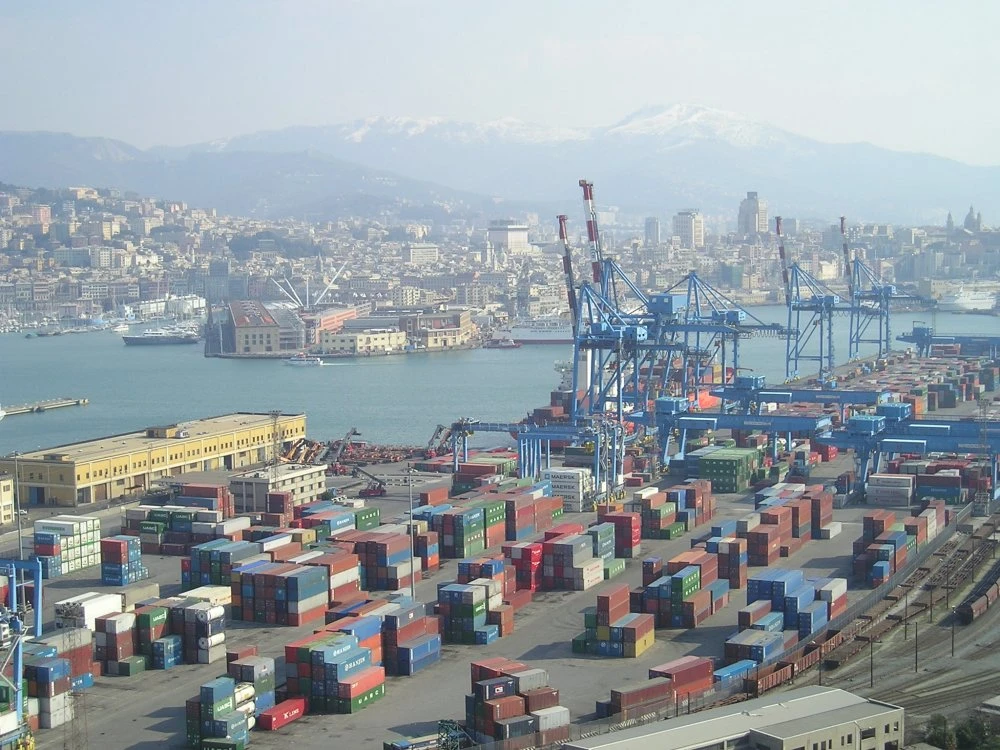 Aerial view of a bustling port with shipping containers, cranes, and city buildings.