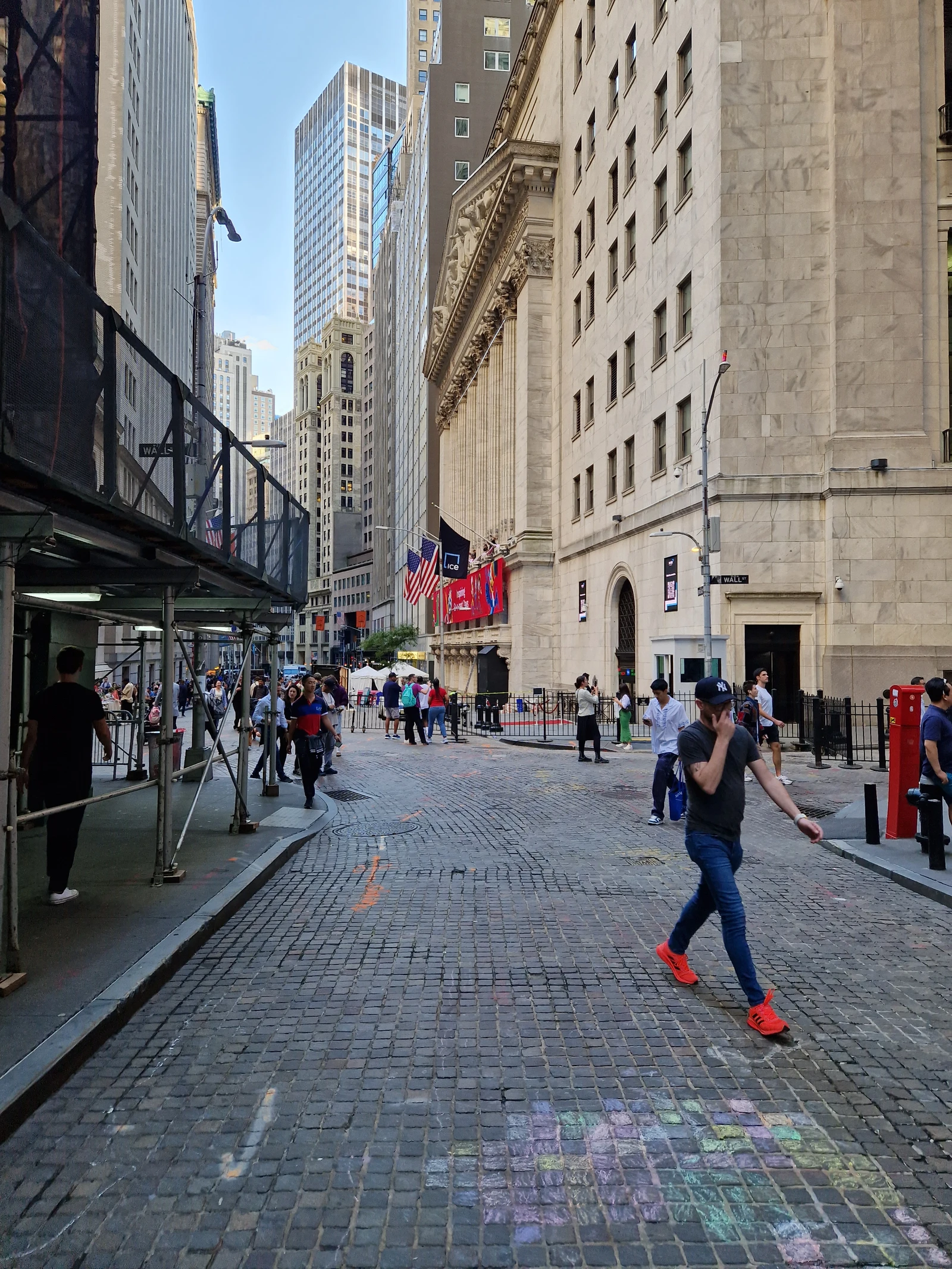 New York Stock Exchange building on Wall Street with people walking on a cobblestone street.