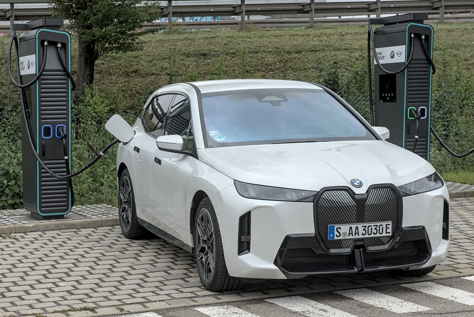 White BMW iX3 electric vehicle parked and connected to a charging station.