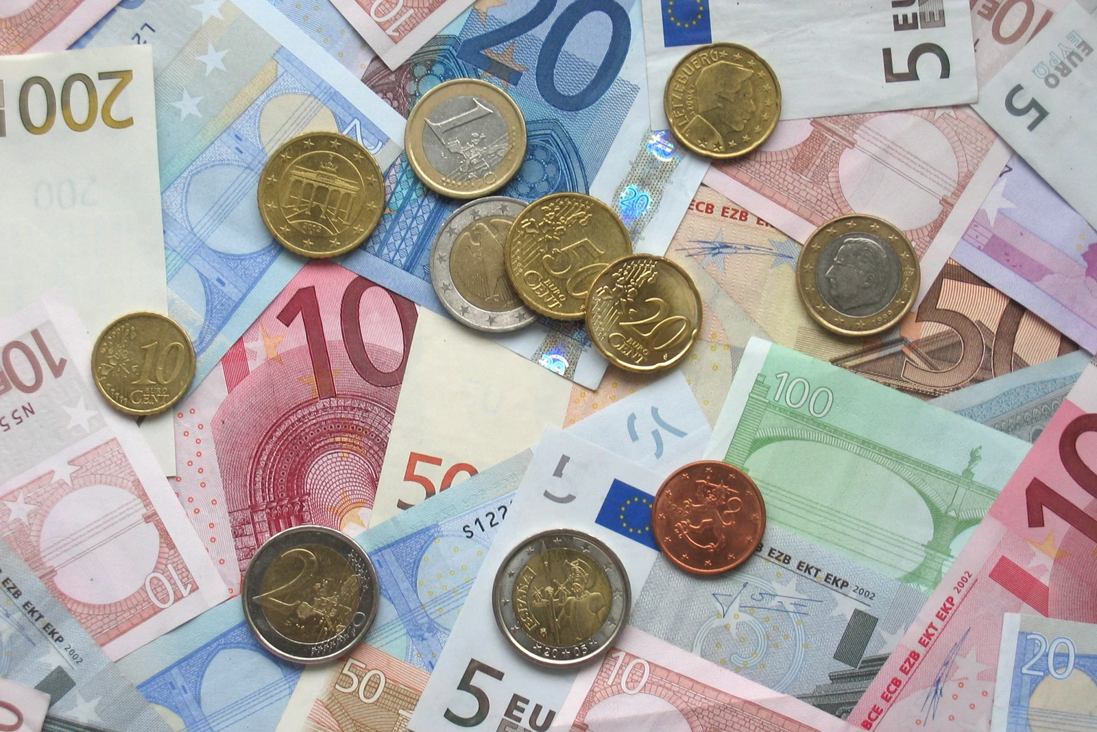 A flat lay of euro coins and various euro banknotes, including 5, 10, 20, 50, 100, and 200 Euro notes.